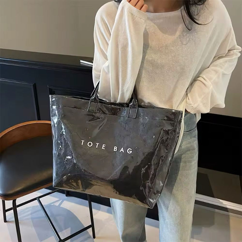 Black transparent jelly tote bag in glossy PVC with bold white letter print – large waterproof handbag for beach, city, or travel use.
