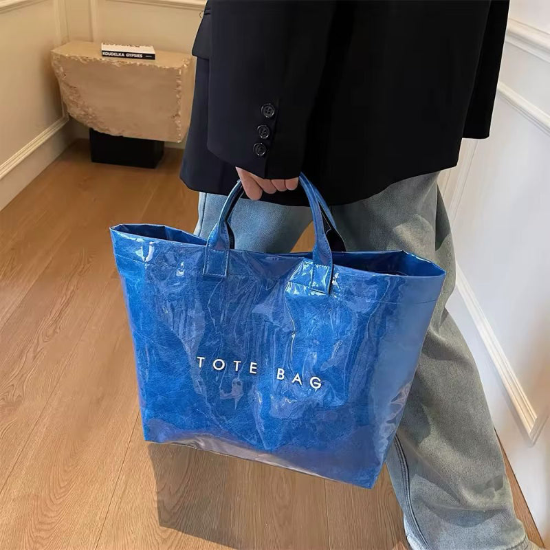 Blue transparent tote bag in waterproof glossy finish – fashionable large-capacity PVC bag with statement print for everyday use.