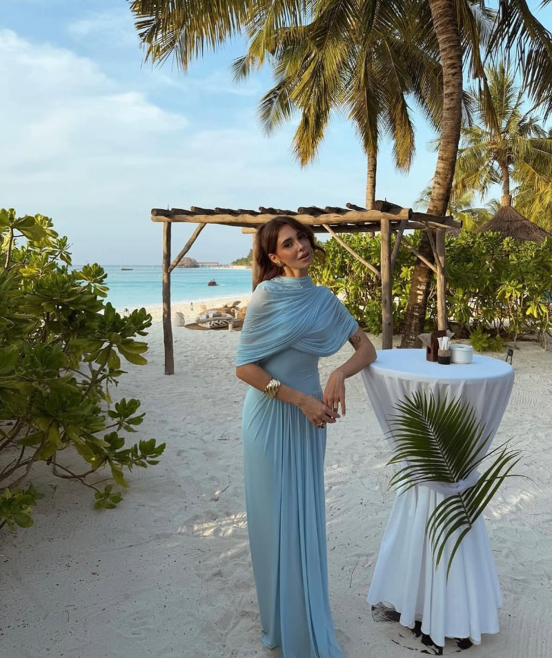 Sky blue draped chiffon evening gown named Chantelle, featuring elegant soft pleats, shoulder wrap detail, and floor-length silhouette – perfect for weddings, galas, and formal events.