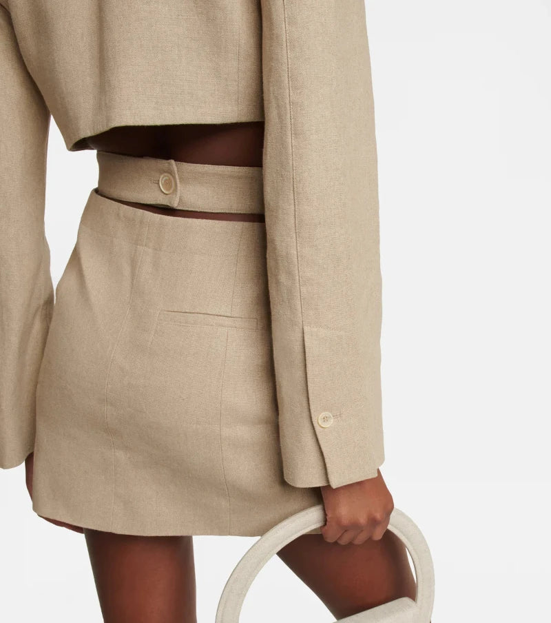 Back view of a beige stretch cotton blazer dress featuring waist cut-outs and decorative button detail.