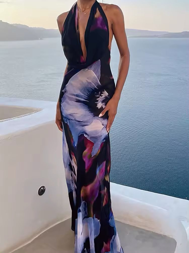 Collage of four images showcasing the “Midnight Bloom” dress. The model wears a backless, deep V-neck floral maxi dress in dark tones with purple, blue, and pink abstract flower prints. Close-up shots highlight the flowy fabric and elegant silhouette. The setting includes minimalist architecture and seaside views.