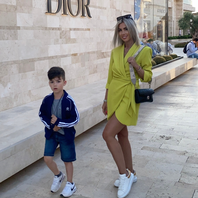 Trendy woman in a breathable yellow wrap dress standing near a high-end fashion store.