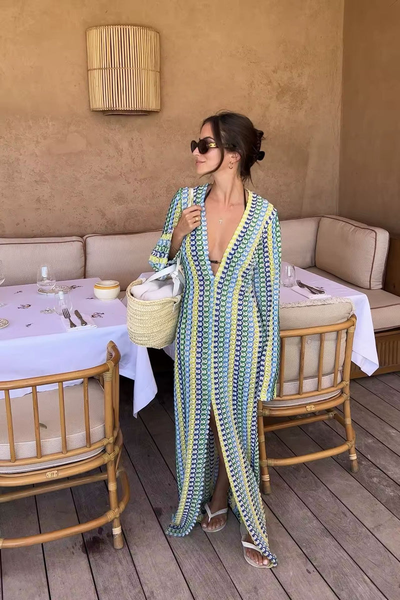 Frau trägt ein buntes Crochet Maxi Dress mit V-Neck, Flare Sleeves und hohem Schlitz – perfekt für Summer Vibes, Boho Chic Looks & Italian Riviera Feelings. Light knit, feminine silhouette, ideal für Beach Clubs & Sunset Moments.