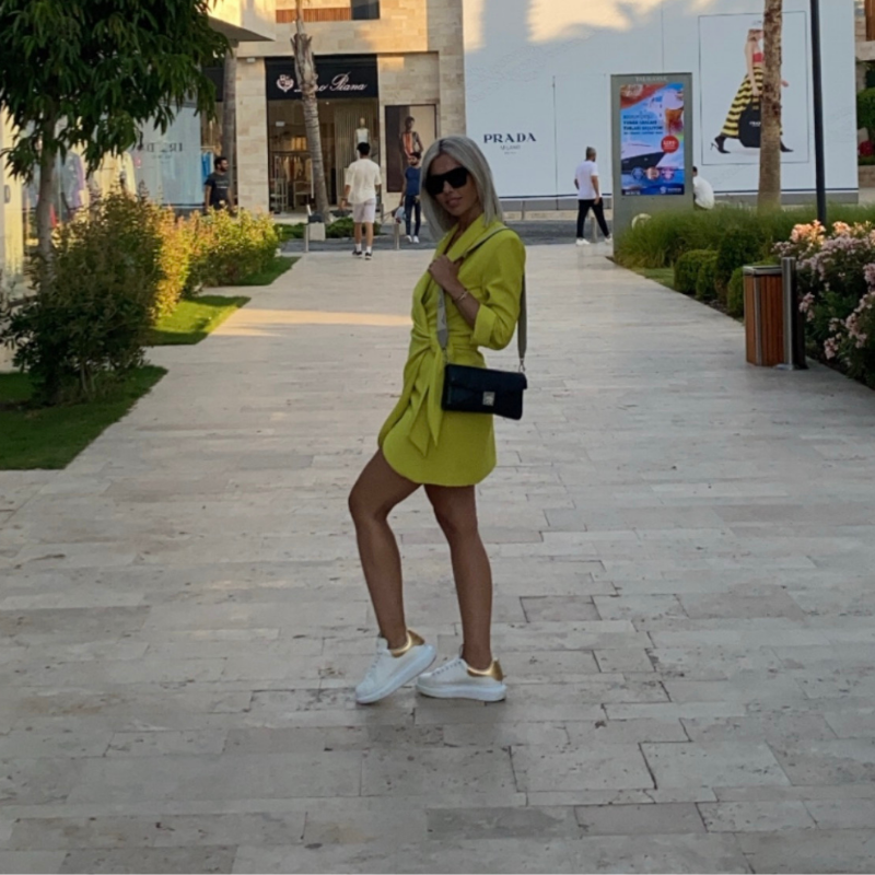Fashionable woman in a Zara-inspired yellow wrap dress posing in a luxury shopping district.