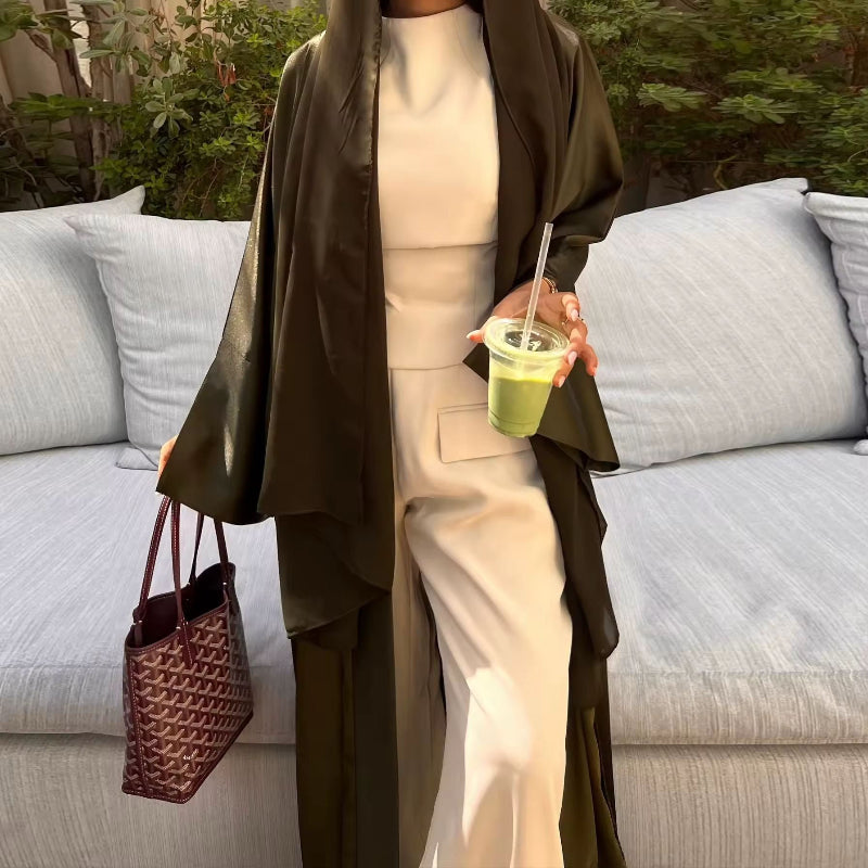 Woman wearing olive green ZAYNA satin abaya over a white outfit, holding a green drink, styled for summer.