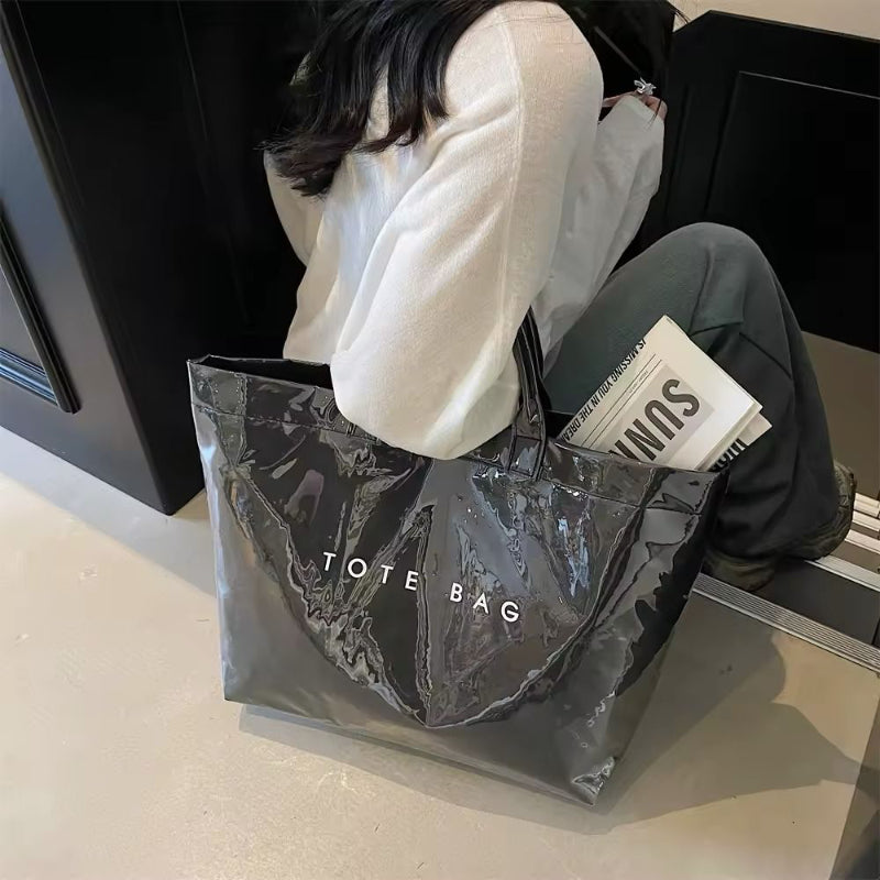 Black transparent jelly tote bag in glossy PVC with bold white letter print – large waterproof handbag for beach, city, or travel use.