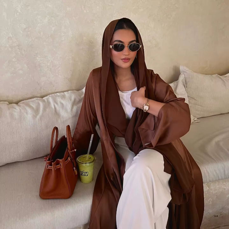 Woman wearing chocolate brown ZAYNA satin abaya over a cream outfit, styled with a designer tote and soft layering.