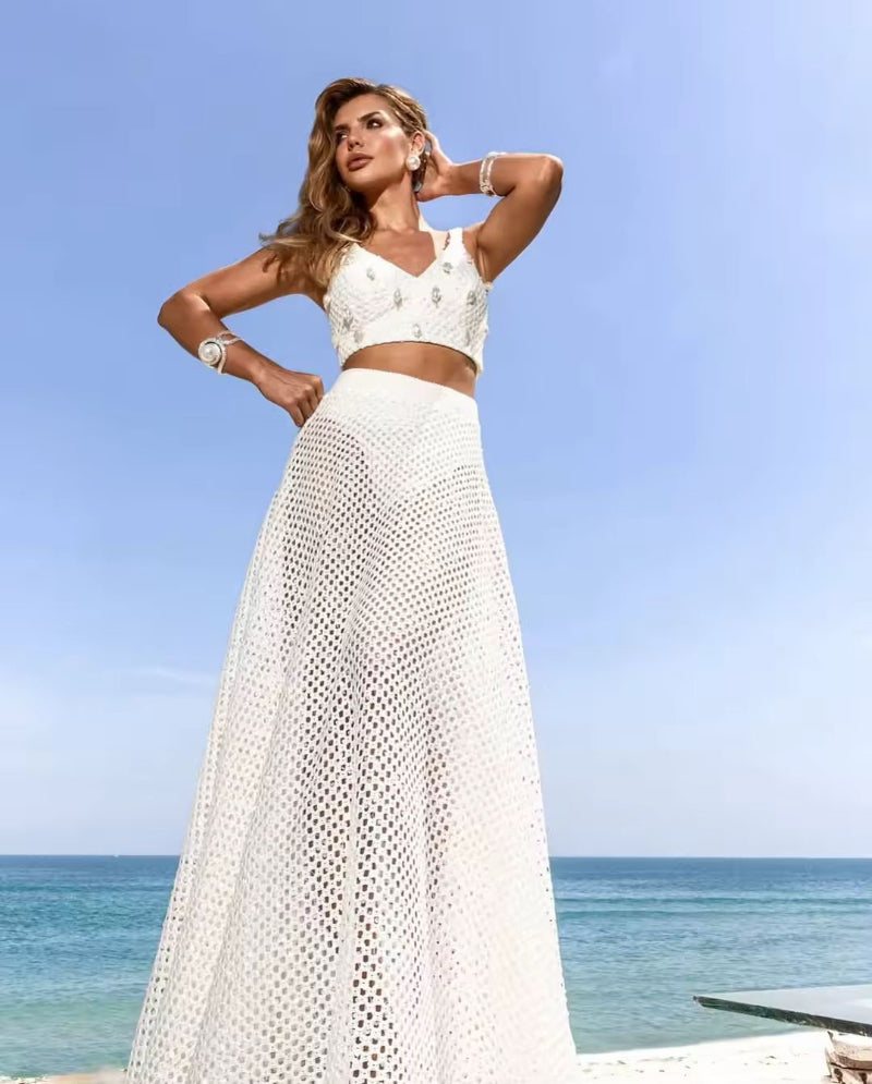 Laid out Amira pearl bikini set including mesh skirt, crochet top, and beach cover-up on beige background
