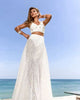 Laid out Amira pearl bikini set including mesh skirt, crochet top, and beach cover-up on beige background
