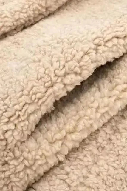 Close-up of teddy coat hem – neatly finished edge of beige long shearling coat with soft lamb fleece material.
