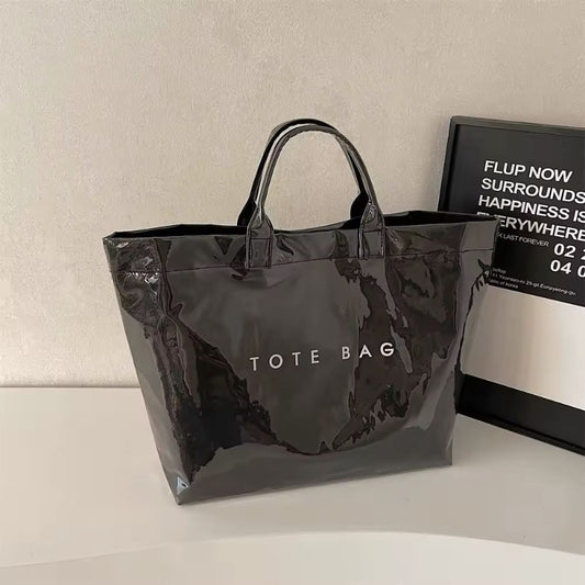 Black transparent jelly tote bag in glossy PVC with bold white letter print – large waterproof handbag for beach, city, or travel use.