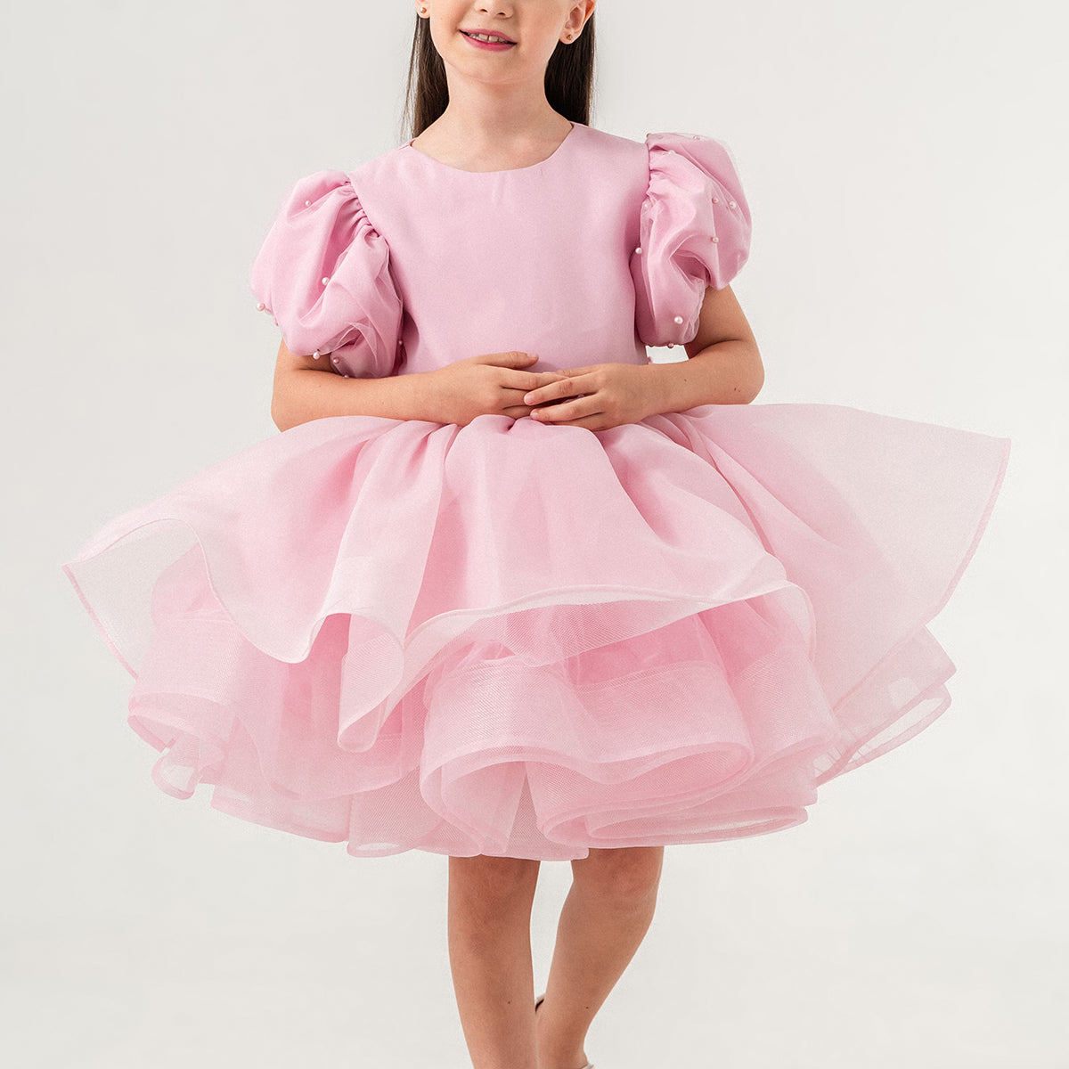 Luxury blush pink princess dress for toddler girls featuring elegant hand-sewn pearl embellishments on puff sleeves, a voluminous layered tulle skirt, and a dramatic oversized bow at the back. Perfect for birthdays, weddings, flower girl moments, and formal occasions. Soft 100% cotton lining for sensitive skin. Couture-inspired, handmade design for unforgettable childhood memories. Ideal for premium kids fashion, special occasion outfits, and baby girl party dresses. Elegant toddler outfit with invisible zi