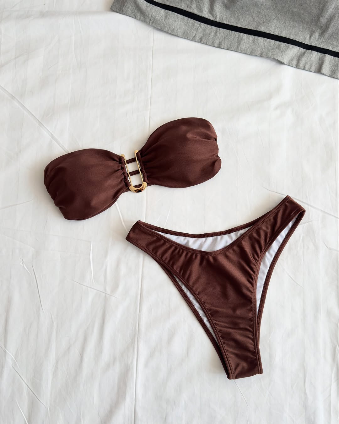 Elegant Brazilian-style bikini set in deep chocolate brown with bandeau top and low-rise bottom, made of seamless nylon-spandex fabric with gold ring detail – displayed on white background.