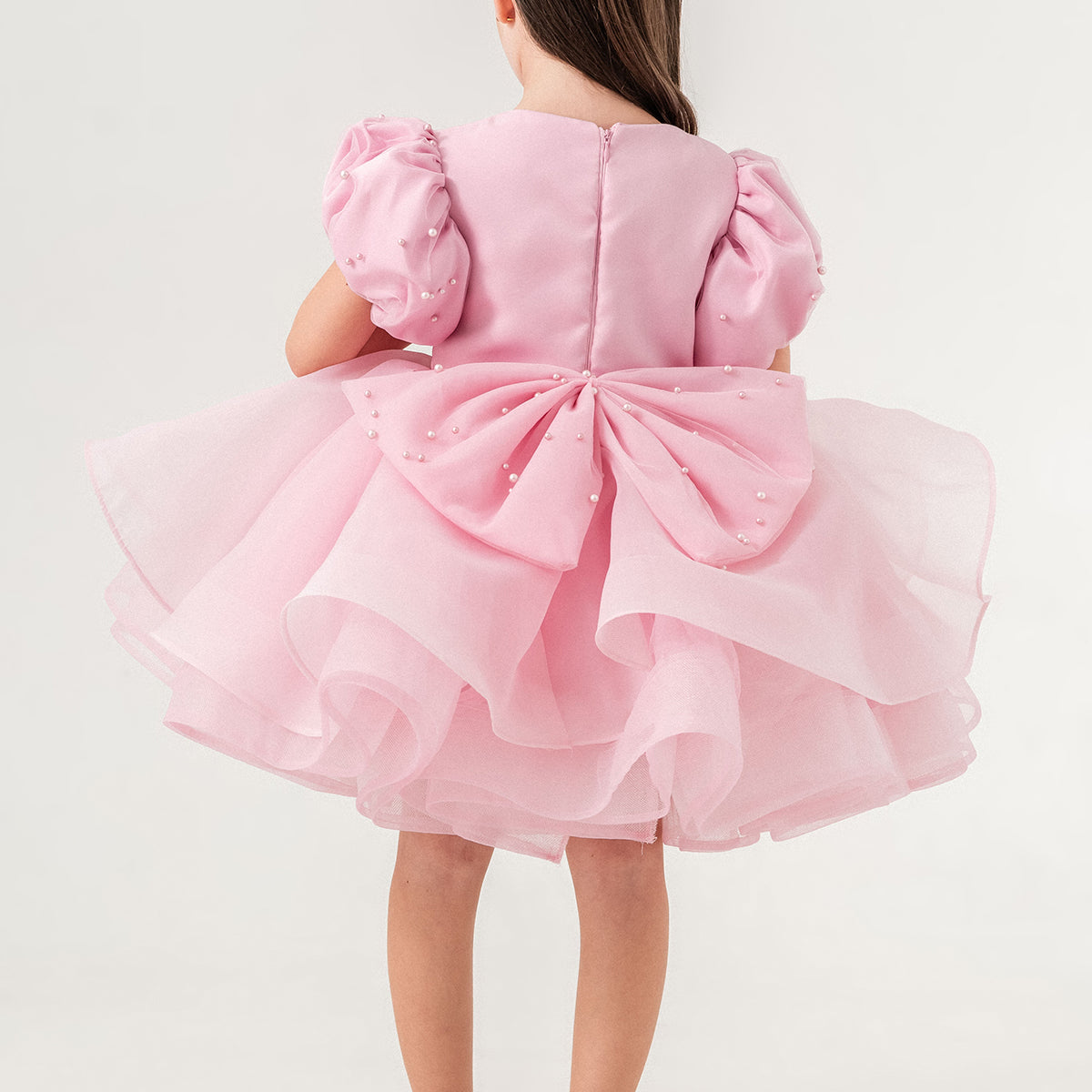 Luxury blush pink princess dress for toddler girls featuring elegant hand-sewn pearl embellishments on puff sleeves, a voluminous layered tulle skirt, and a dramatic oversized bow at the back. Perfect for birthdays, weddings, flower girl moments, and formal occasions. Soft 100% cotton lining for sensitive skin. Couture-inspired, handmade design for unforgettable childhood memories. Ideal for premium kids fashion, special occasion outfits, and baby girl party dresses. Elegant toddler outfit with invisible zi