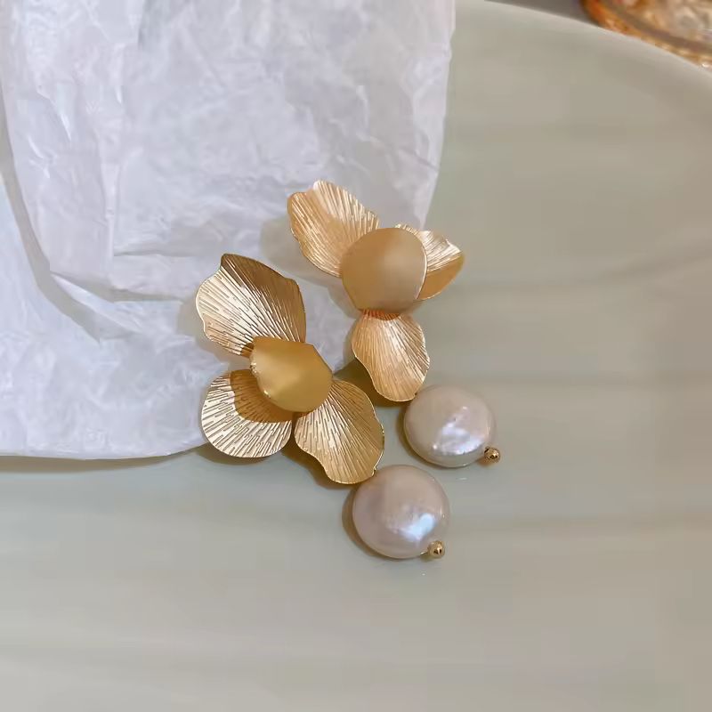 Close-up of textured gold flower earrings with hanging freshwater pearl – elegant wedding and evening accessory
