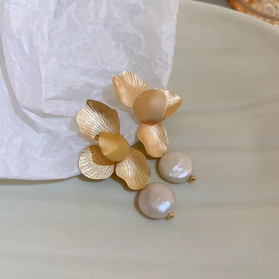 Close-up of textured gold flower earrings with hanging freshwater pearl – elegant wedding and evening accessory
