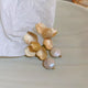 Close-up of textured gold flower earrings with hanging freshwater pearl – elegant wedding and evening accessory
