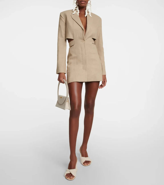 Woman wearing a beige cut-out blazer dress with V-neck, long sleeves, and tailored fit. Side cut-outs and single-button closure complete the chic design.
