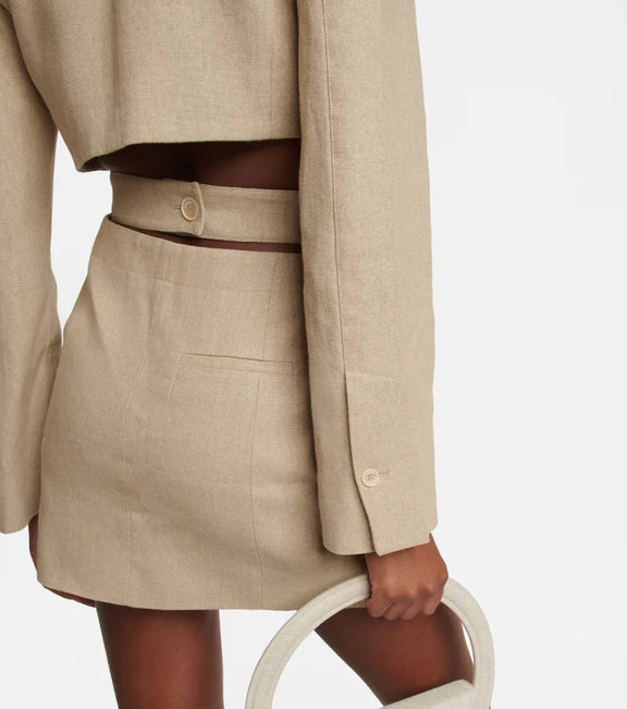 Back view of a beige stretch cotton blazer dress featuring waist cut-outs and decorative button detail.