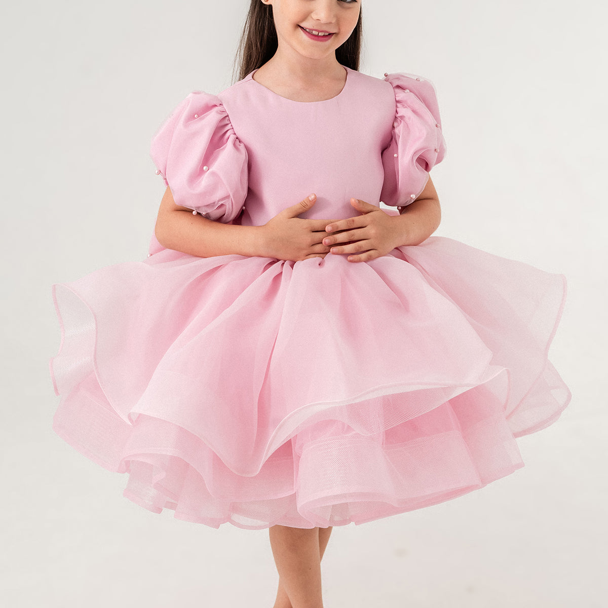 Luxury blush pink princess dress for toddler girls featuring elegant hand-sewn pearl embellishments on puff sleeves, a voluminous layered tulle skirt, and a dramatic oversized bow at the back. Perfect for birthdays, weddings, flower girl moments, and formal occasions. Soft 100% cotton lining for sensitive skin. Couture-inspired, handmade design for unforgettable childhood memories. Ideal for premium kids fashion, special occasion outfits, and baby girl party dresses. Elegant toddler outfit with invisible zi