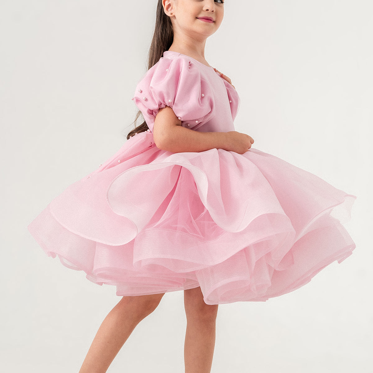 Luxury blush pink princess dress for toddler girls featuring elegant hand-sewn pearl embellishments on puff sleeves, a voluminous layered tulle skirt, and a dramatic oversized bow at the back. Perfect for birthdays, weddings, flower girl moments, and formal occasions. Soft 100% cotton lining for sensitive skin. Couture-inspired, handmade design for unforgettable childhood memories. Ideal for premium kids fashion, special occasion outfits, and baby girl party dresses. Elegant toddler outfit with invisible zi