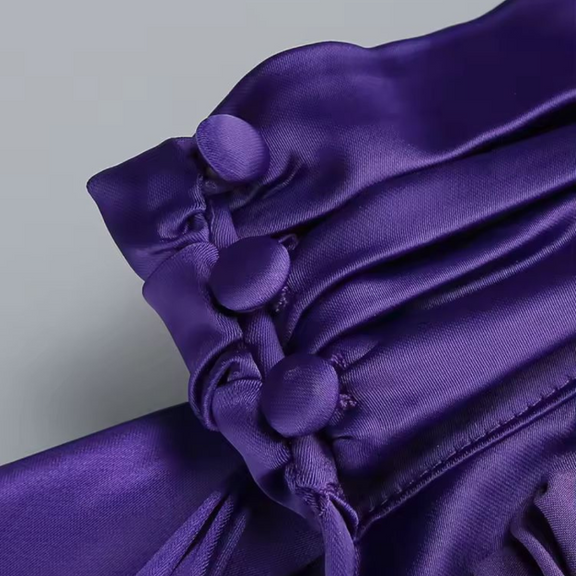 Side profile of woman in glamorous purple evening dress with draped fabric and open back
	