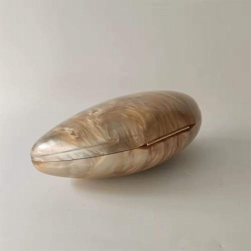 Bridal evening clutch in shell-inspired design with smooth acrylic surface and luxurious gold accents.
