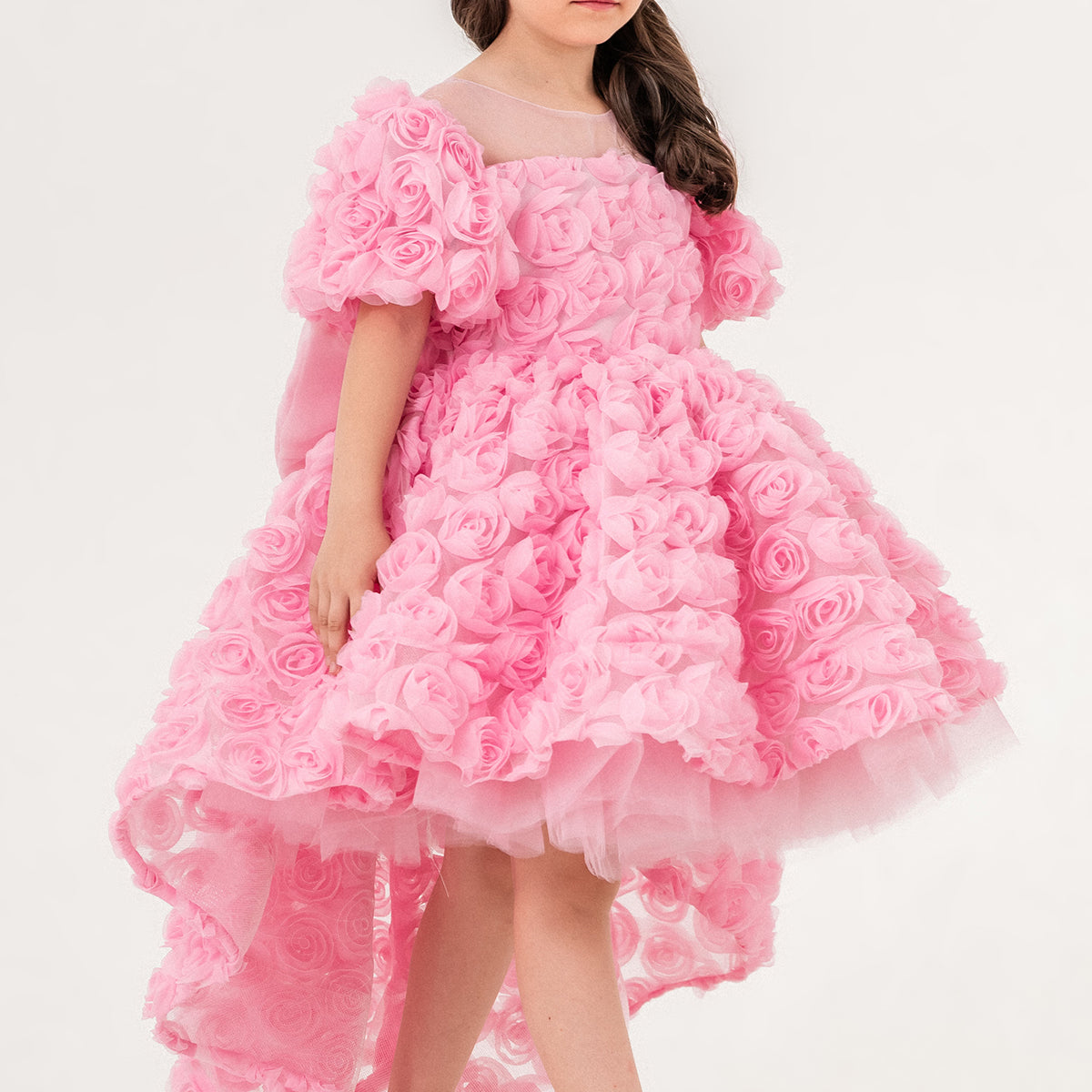 Young girl wearing a luxury pink 3D rose dress with puff sleeves and a high-low tulle skirt, perfect for birthdays, weddings, and special occasions. Handmade in Turkey by Chic and Charm, this elegant flower girl dress features premium embroidered tulle, cotton lining for sensitive skin, and couture-level details. Ideal for formal events, stylish photoshoots, and princess-inspired outfits. Luxury kids fashion - designer girls dress - handmade kidswear - pastel pink occasion dress.