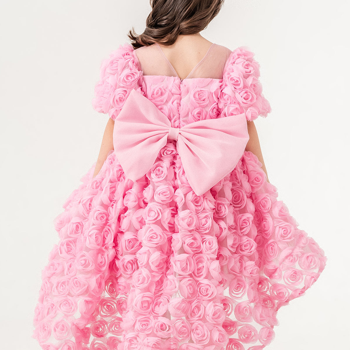 Young girl wearing a luxury pink 3D rose dress with puff sleeves and a high-low tulle skirt, perfect for birthdays, weddings, and special occasions. Handmade in Turkey by Chic and Charm, this elegant flower girl dress features premium embroidered tulle, cotton lining for sensitive skin, and couture-level details. Ideal for formal events, stylish photoshoots, and princess-inspired outfits. Luxury kids fashion - designer girls dress - handmade kidswear - pastel pink occasion dress.
