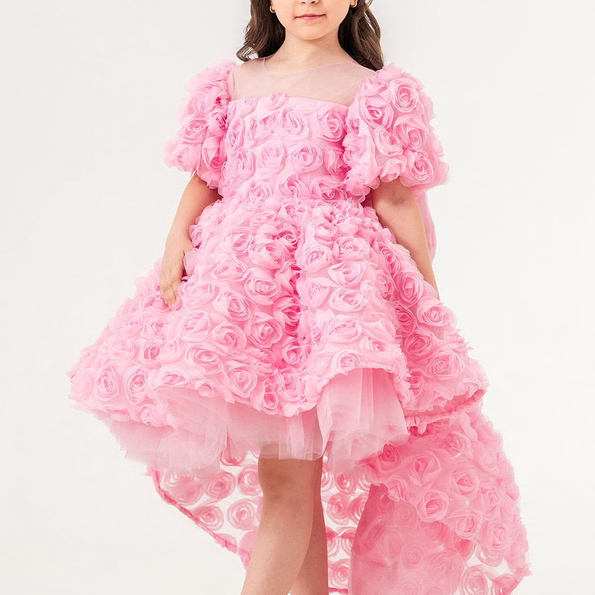 Young girl wearing a luxury pink 3D rose dress with puff sleeves and a high-low tulle skirt, perfect for birthdays, weddings, and special occasions. Handmade in Turkey by Chic and Charm, this elegant flower girl dress features premium embroidered tulle, cotton lining for sensitive skin, and couture-level details. Ideal for formal events, stylish photoshoots, and princess-inspired outfits. Luxury kids fashion - designer girls dress - handmade kidswear - pastel pink occasion dress.