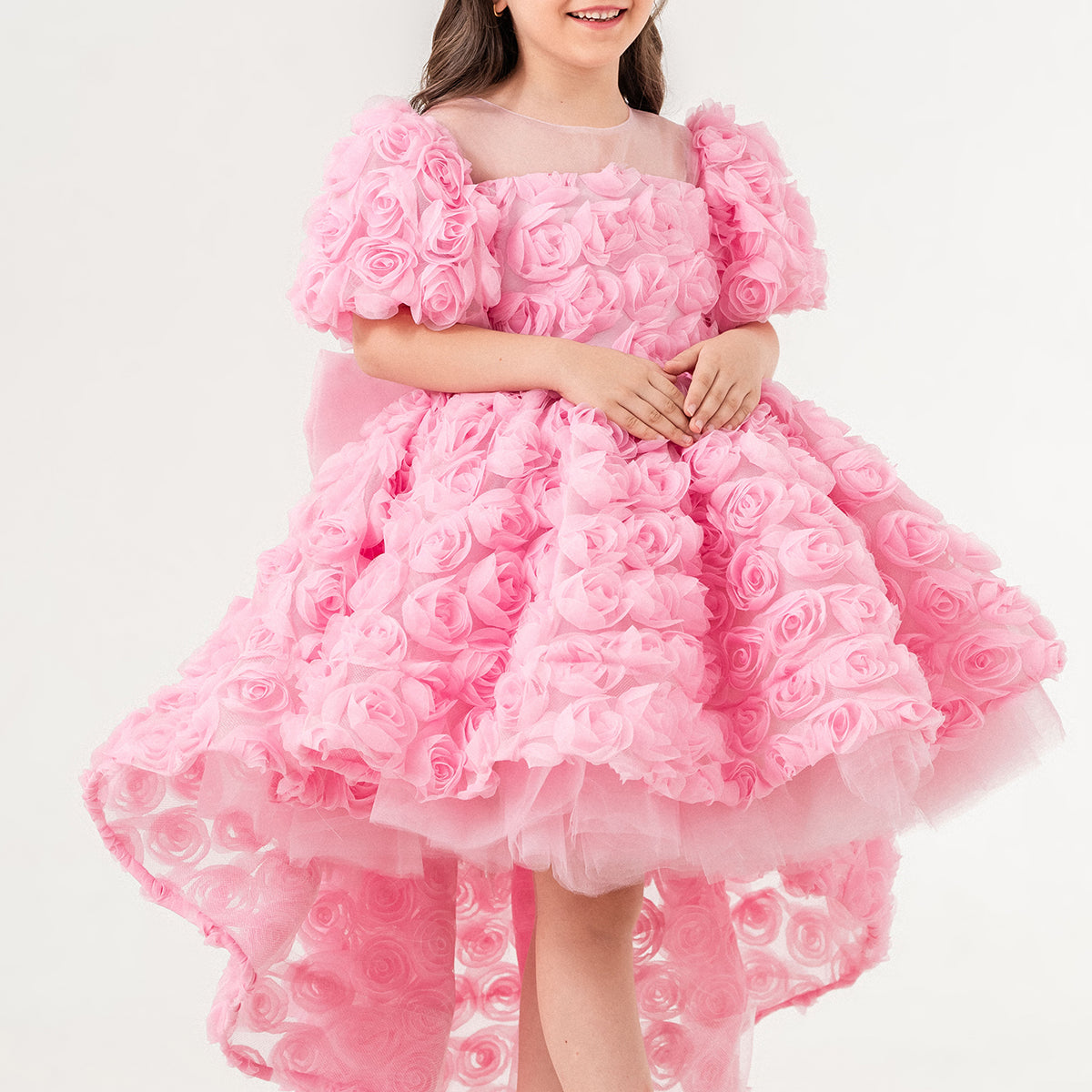 Young girl wearing a luxury pink 3D rose dress with puff sleeves and a high-low tulle skirt, perfect for birthdays, weddings, and special occasions. Handmade in Turkey by Chic and Charm, this elegant flower girl dress features premium embroidered tulle, cotton lining for sensitive skin, and couture-level details. Ideal for formal events, stylish photoshoots, and princess-inspired outfits. Luxury kids fashion -designer girls dress - handmade kidswear - pastel pink occasion dress.