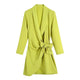 Woman wearing a vibrant neon yellow wrap dress with long sleeves and white sneakers in front of a Dior store.
