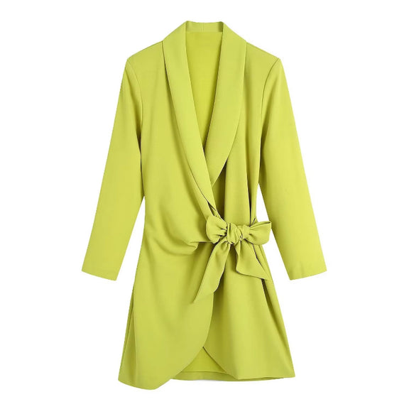 Knee-length neon yellow wrap dress for women styled with a black bag and casual white trainers.
