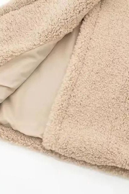 Close-up of beige teddy coat fabric – soft, fluffy lamb fleece texture showing high-quality faux shearling material.
