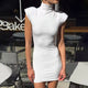 Woman wearing white high-neck sleeveless mini dress with ruched shoulders, sitting in sunlight.
