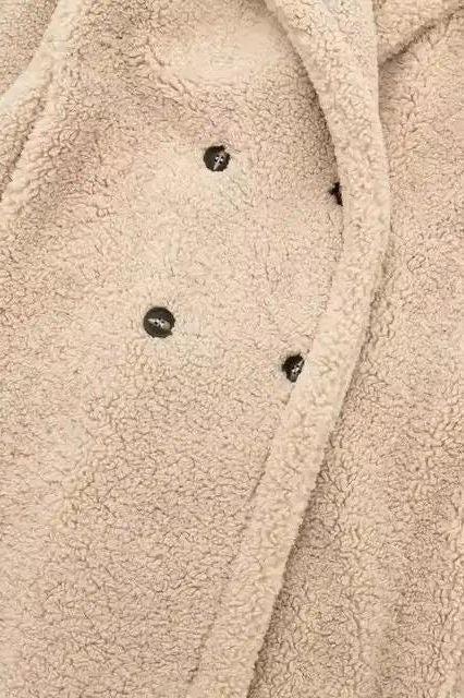 Detailed view of teddy coat button – premium double-breasted button design on thick beige shearling fabric.

