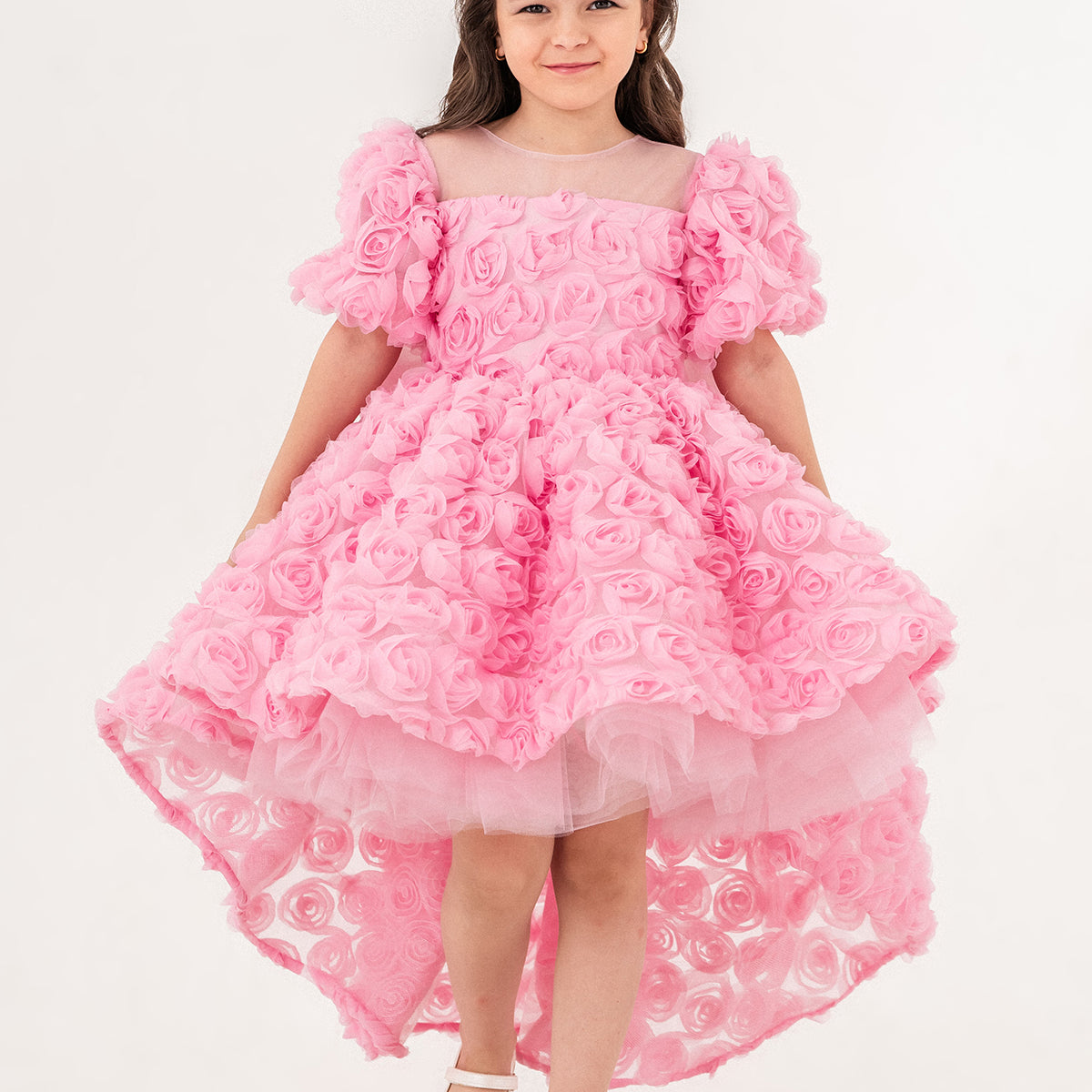 Young girl wearing a luxury pink 3D rose dress with puff sleeves and a high-low tulle skirt, perfect for birthdays, weddings, and special occasions. Handmade in Turkey by Chic and Charm, this elegant flower girl dress features premium embroidered tulle, cotton lining for sensitive skin, and couture-level details. Ideal for formal events, stylish photoshoots, and princess-inspired outfits. Luxury kids fashion - designer girls dress - handmade kidswear - pastel pink occasion dress.