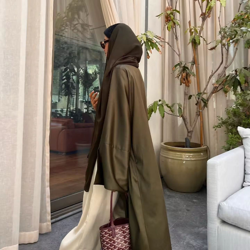 Woman wearing olive green ZAYNA satin abaya over a white outfit, holding a green drink, styled for summer.
